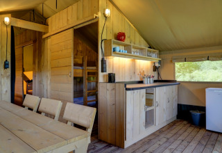 Interior of a glamping safari tent at Domaine La Barbe in France, featuring wooden furniture and kitchenette.