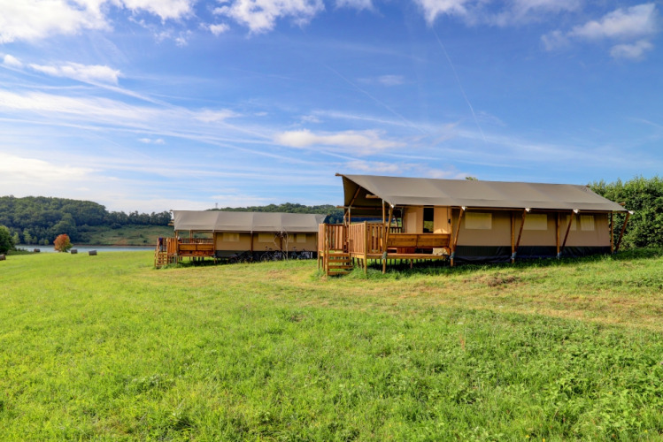 Tende safari glamping al Domaine La Barbe in Francia, situate su un prato verde con vista su lago e foresta.