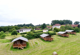 Glamping safaritenten op Domaine La Barbe in Frankrijk, op een groene wei met huizen op de achtergrond.
