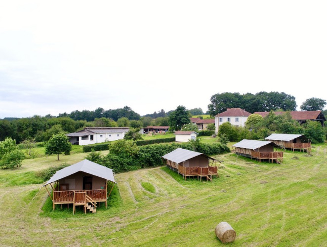 Luksustelte på grøn mark ved Domaine La Barbe i Frankrig, med huse i baggrunden og rullende hø på marken.