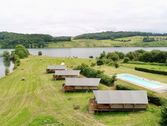 Glamping safari tents at Domaine La Barbe, France, overlooking a lake and a swimming pool in nature.