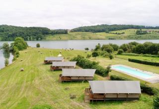 Glamping safari tents at Domaine La Barbe, France, overlooking a lake and a swimming pool in nature.