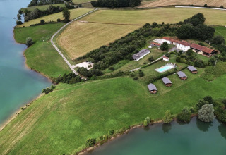 Aerial view of glamping site with safari tents, pool, and lake at Domaine La Barbe, France, surrounded by nature.