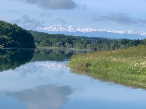 Roligt landskab nær Lalanne-Arqué i Occitanie, Frankrig, med sø, træer og snedækkede bjerge i det fjerne.