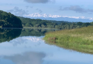 Idyllische Landschaft bei Lalanne-Arqué in Okzitanien, Frankreich, mit See, Bäumen und schneebedeckten Bergen.