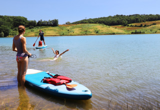 People paddleboarding and swimming in the lake at Domaine La Barbe holiday park in Occitanie, France.
