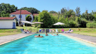Outdoor swimming pool with guests, sun loungers, and umbrellas at Domaine La Barbe holiday park in Occitanie, France.