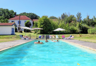 Piscina all'aperto con ospiti, lettini e ombrelloni presso il parco vacanze Domaine La Barbe in Occitania, Francia.