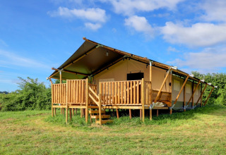 Glamping safaritent met houten terras op een veld, onder een blauwe lucht, ideaal voor luxe kamperen.