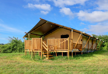 Tienda safari glamping con porche de madera en un campo verde, ideal para una experiencia de camping lujosa.