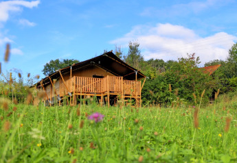Tenda safari glamping con terrazza in legno a Domaine La Barbe, Francia, circondata da prato fiorito.