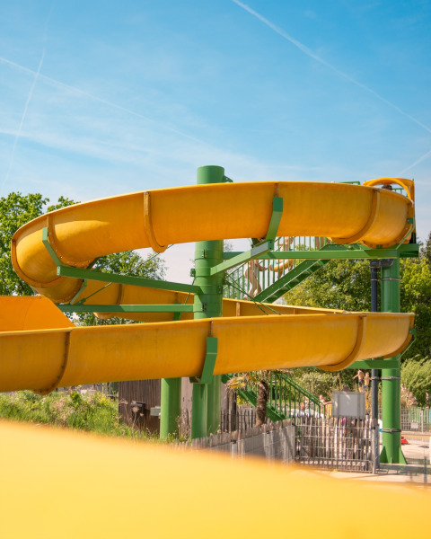 Yellow water slide at a glamping accommodation on a sunny day with green trees and blue sky around.