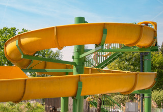 Yellow water slide at a glamping accommodation on a sunny day with green trees and blue sky around.