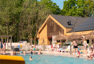 Piscina al aire libre junto a una tienda safari, con gente tomando el sol y nadando bajo el cielo azul.