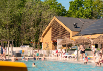 Udendørs swimmingpool ved et safari telt med folk der soler sig og svømmer under blå himmel.