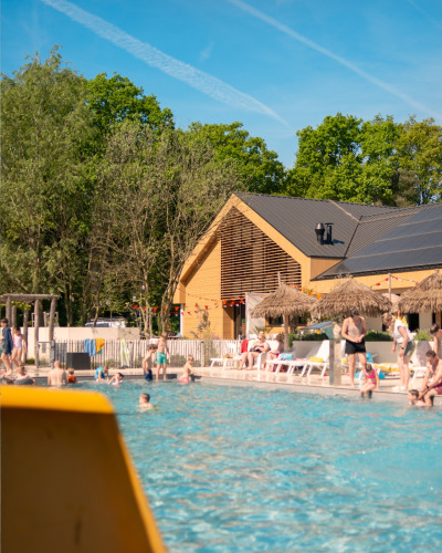 Piscine extérieure devant une tente safari avec des personnes bronzant et nageant sous un ciel bleu clair.