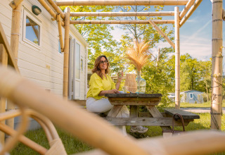 Femme assise à une table de pique-nique devant une tiny house à Zomerhuisjes, Beloofde Land, Pays-Bas, été.
