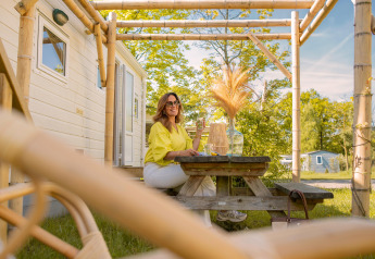 Kvinde sidder ved et picnicbord foran et lille hus i Zomerhuisjes, Beloofde Land, Nederlandene, om sommeren.