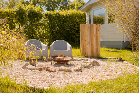 Two modern chairs and a fire pit on gravel beside a tiny house at Beloofde Land, Netherlands.