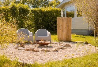 Zwei moderne Stühle und eine Feuerstelle im Kiesbereich neben einem Tiny House in Beloofde Land, Niederlande.