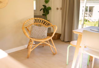 Bright tiny house interior at Zomerhuisjes in Beloofde Land, Netherlands, with a wicker chair and cushion.