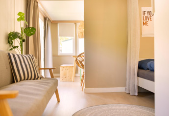 Bright interior of a Zomerhuisjes tiny house at Beloofde Land, Netherlands, featuring sofa and bed.