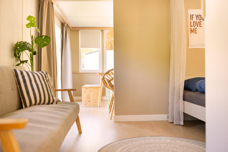 Interior luminoso de una tiny house Zomerhuisjes en Beloofde Land, Países Bajos, con sofá y cama.
