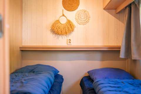 Two single beds with blue bedding in a tiny house at Zomerhuisjes, Beloofde Land, Netherlands.