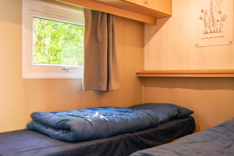 Dormitorio de una tiny house en Zomerhuisjes, Beloofde Land, Países Bajos, con ventana y ropa de cama azul.
