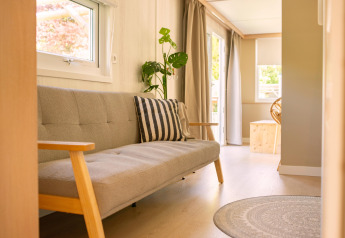 Lyst og hyggeligt interiør i et tiny house med grå sofa, stribet pude og planter, Zomerhuisjes, Holland.