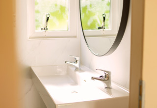 Petite salle de bain avec miroir rond et double robinet à Zomerhuisjes, Beloofde Land, Pays-Bas.