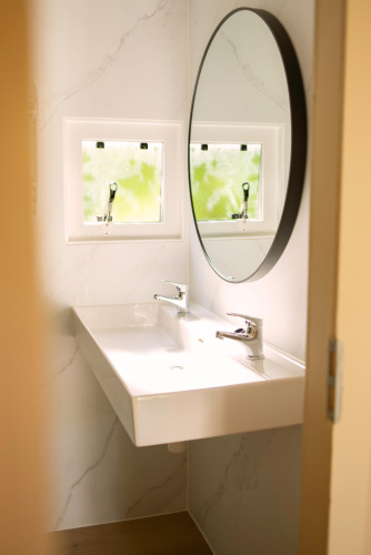 Tiny bathroom at Zomerhuisjes in Beloofde Land, Netherlands, featuring round mirror and twin faucets.