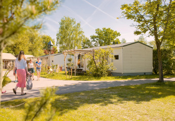 Familie går ved Zomerhuisjes tiny house på Beloofde Land i Holland, omgivet af grønne træer og sommerstemning.