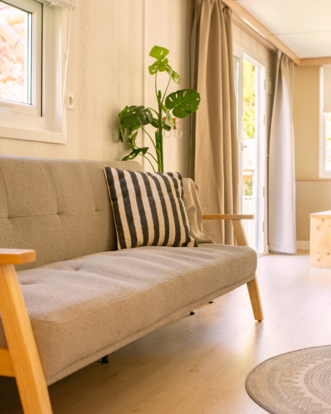 Bright, minimalist tiny house living room at Zomerhuisjes, Netherlands, with sofa, striped pillow and plant.