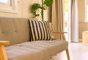 Helles, modernes Wohnzimmer mit beigem Sofa, gestreiftem Kissen, grüner Pflanze und viel Licht, Zomerhuisjes NL.