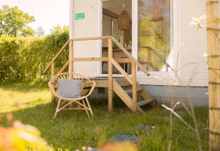 Tiny house Zomerhuisjes at Beloofde Land in the Netherlands, with a chair and cushion in the grassy yard.