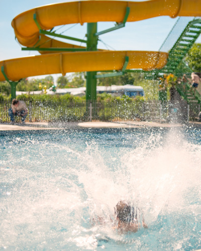 A child splashes into a pool beneath a yellow slide at Boerderij huisje, Beloofde Land in the Netherlands.