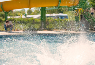 Un enfant fait une grande éclaboussure dans une piscine près d'un toboggan jaune à Boerderij huisje, Beloofde Land.