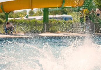 Een kind plonst met veel water in het zwembad onder een gele glijbaan bij Boerderij huisje, Beloofde Land.