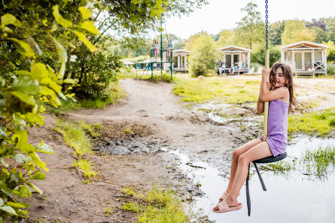 Une fille sur une balançoire devant une tente safari Boerderij à Beloofde Land, Pays-Bas, entourée de nature.