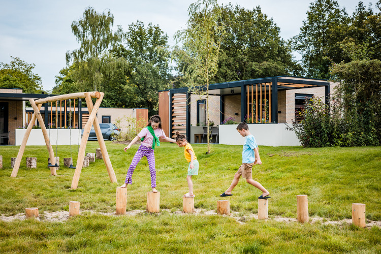Kinder spielen draußen auf Holzstämmen vor einem Safarizelt bei Boerderij huisje im Beloofde Land, Niederlande.