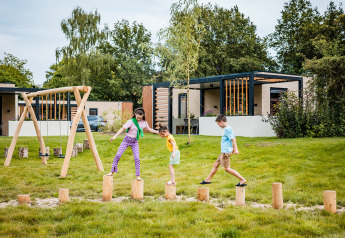 Kinderen spelen buiten op houten palen voor een safaritent bij Boerderij huisje, Beloofde Land, Nederland.