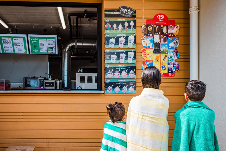 Three children wrapped in towels look at an ice cream menu at a food stand at Boerderij huisje, Beloofde Land.