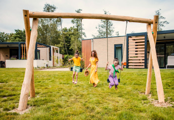 Een moeder en twee kinderen spelen bij een safaritent op Beloofde Land in Nederland, buiten in het groen.