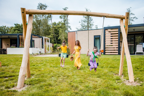 A mother and two kids play on a swing set near a safari tent at Beloofde Land in the Netherlands, outdoors.