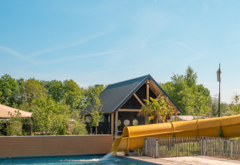 Piscina exterior con tobogán amarillo y flotadores en Jippi Tippi, Beloofde Land, Países Bajos, día soleado.