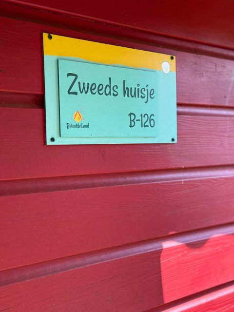 Et skilt på en rød trævæg, der viser navnet 'Zweeds huisje' og værelsesnummer B-126 i Beloofde Land.