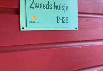 Un letrero en una pared roja dice 'Zweeds huisje' y el número de habitación B-126 en Beloofde Land, Países Bajos.
