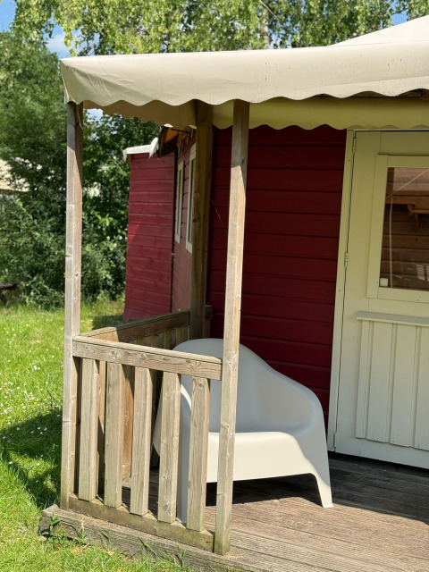 En solbeskinnet veranda med hvid stol foran en rød træhytte ved Zweedse Huisjes i Beloofde Land.