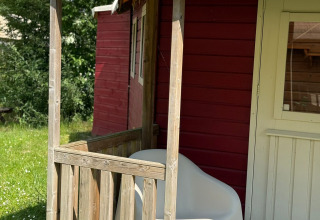 Sunny porch with a white chair in front of a red cabin at Zweedse Huisjes, Beloofde Land, Netherlands.